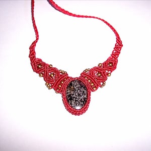 May include: A red macrame necklace with a dark grey oval stone pendant and gold beads.