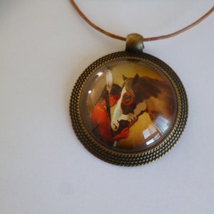 Peut inclure: Un collier avec un pendentif rond en bronze et un dôme en verre représentant une peinture d'un homme amérindien et d'un cheval. Le cheval est brun et blanc avec un motif peint bleu et blanc sur son visage. L'homme porte une coiffe à plumes rouge et brune.