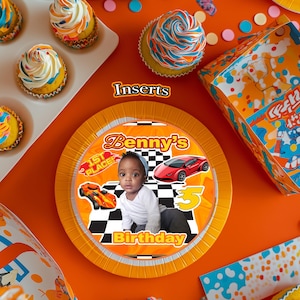 Op de afbeelding: Een oranje en gele verjaardagspartyscène met cupcakes, een bord en een doos. Het bord toont een kind, raceauto's en de tekst "Benny's Birthday". Cupcakes hebben blauwe, oranje en witte glazuur.