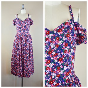 May include: A vintage floral print dress with a sweetheart neckline and off-the-shoulder sleeves. The dress features a vibrant pattern of red, pink, and white flowers on a navy blue background. The dress is displayed on a mannequin.