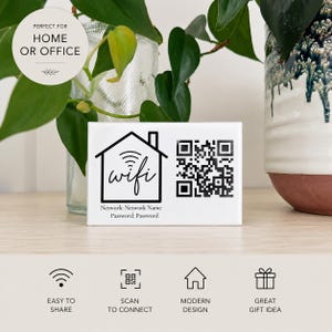 May include: A rectangular white sign featuring a black house icon with a wifi symbol, the word wifi, a QR code, and the text Network: Network Name and Password: Password. The sign is positioned in front of a glass vase with green leaves.