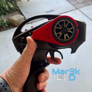 May include: Black remote control with a red trigger and a black and gold wheel on the top. The remote control has a silver label that says "Traxxas 2.4GHz".