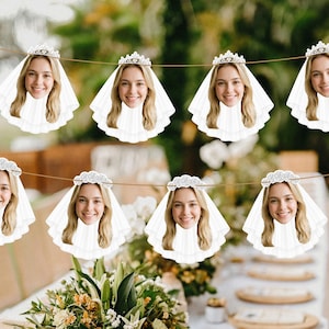 May include: A decorative party banner featuring a repeating cutout of a smiling person with blonde hair wearing a white bridal veil and a silver tiara. The cutouts are strung together on a thin brown cord, creating a festive garland for events.