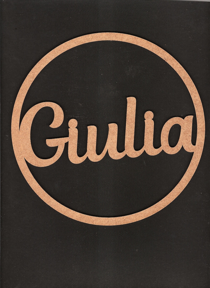 May include: A wooden circle with the name "Giulia" cut out in a cursive font. The circle is a light brown color and the background is black.