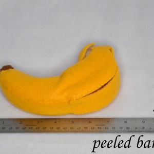 May include: A yellow felt banana with a brown stem, measuring approximately 7 inches long. The banana is peeled open, revealing a white felt lining.