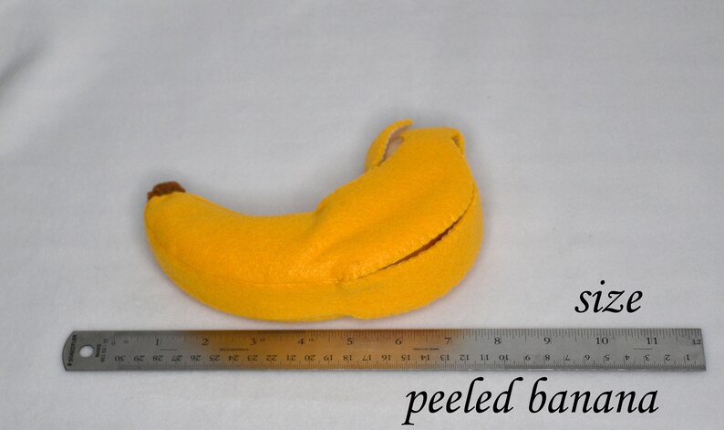 May include: A yellow felt banana with a brown stem, measuring approximately 7 inches long. The banana is peeled open, revealing a white felt lining.