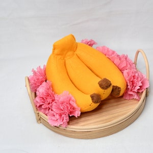 May include: A bunch of yellow felt bananas in a wooden tray with pink felt carnations around the edge.