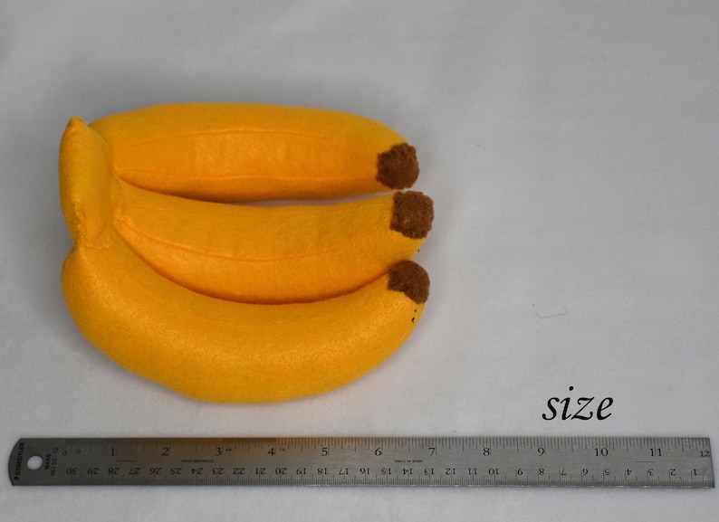 May include: Three yellow felt bananas with brown felt stems, measured against a ruler, showing they are approximately 7 inches long.