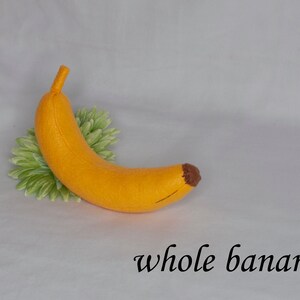 May include: A felt banana toy, yellow with a brown tip, on a white background with green leaves.