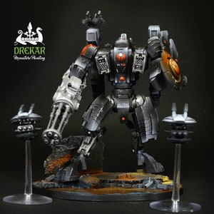 May include: A detailed miniature of a futuristic robot with a large gun arm and shield. The robot is primarily gray with orange and black accents. Two smaller drone-like figures stand nearby. The base is textured with a rocky appearance. The text "DREKAR Miniature Painting" is visible.