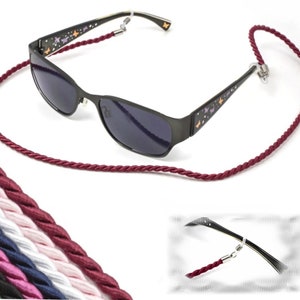 May include: Burgundy braided cord eyeglasses retainer with a pair of black sunglasses with butterfly designs. The sunglasses have dark lenses. The image also shows a variety of colors of the same cord.