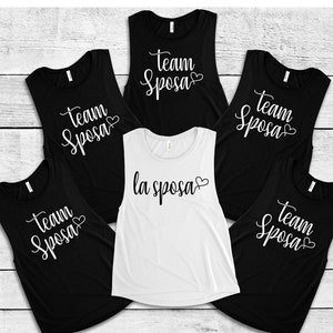 Op de afbeelding: Vijf tanktops zonder mouwen met de tekst "Team Sposa" in witte letters met een klein hartje. Een tanktop is wit met de tekst "la sposa" in zwarte letters met een klein hartje.
