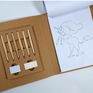 Peut inclure: Un kit de bricolage dans un &eacute;tui en carton brun, contenant six crayons en bois et deux gommes. Un livre de coloriage avec un contour de licorne est ouvert. Le kit est pour les activit&eacute;s cr&eacute;atives.