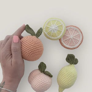 Peut inclure: Ensemble de fruits crochetés comprenant une orange, un citron, une pêche et deux tranches d'agrumes. Les jouets faits à la main sont dans des tons d'orange, de jaune et de rose, avec des feuilles vertes. Les tranches de fruits ont des détails blancs.