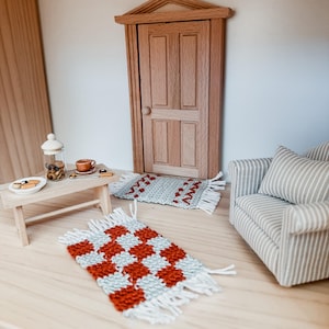May include: Miniature dollhouse furniture set with a wooden door, a small sofa with a striped pillow, a coffee table with a plate of cookies, and two woven rugs. The rugs have red and white patterns.