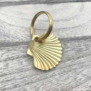 May include: A gold-coloured seashell keyring with a ring attached. The seashell has a detailed design and is a popular beach-themed accessory.