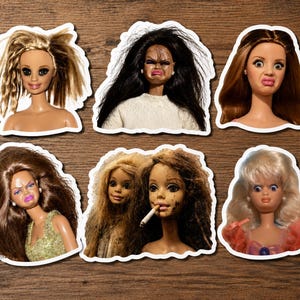 May include: A collection of six die-cut stickers featuring various doll heads with distinct facial expressions and hairstyles, including one doll with messy blonde hair, one with dark hair, one with brown hair, and one holding a cigarette.