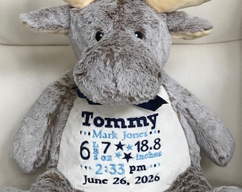 May include: A plush gray moose stuffed animal with tan antlers and a dark blue ribbon around its neck. The white belly features embroidered text: Tommy, Mark Jones, 6 lbs 7 oz, 18.8 inches, 2:33 pm, and June 26, 2026, with blue stars.