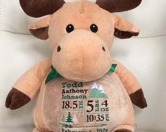 May include: A tan plush moose toy with dark brown antlers and hooves, featuring a green ribbon around its neck. The chest is embroidered with the name Todd Anthony Johnson, birth details including 18.5 in, 5 lbs 4 oz, 10:35 PM, and February 6, 2020.