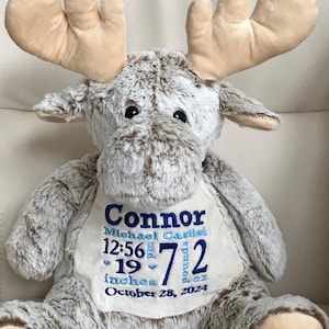 Peut inclure: Une peluche en forme d'élan avec une fourrure douce tachetée de brun et de blanc et des bois beiges. Un écusson en tissu blanc sur la poitrine porte le texte brodé en bleu : Connor, Michael Castiel, 12:56 pm, 19 inches, 7 pounds 2 oz, 28 octobre 2024.