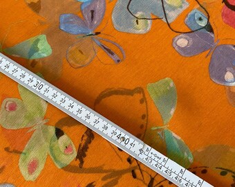 May include: Orange fabric with a butterfly pattern in shades of blue, green, and purple. A white ruler with black markings is placed diagonally across the fabric, measuring up to 51 inches.
