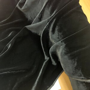 May include: Black velvet fabric with a smooth, soft texture. The fabric is folded and draped, showing its luxurious feel.