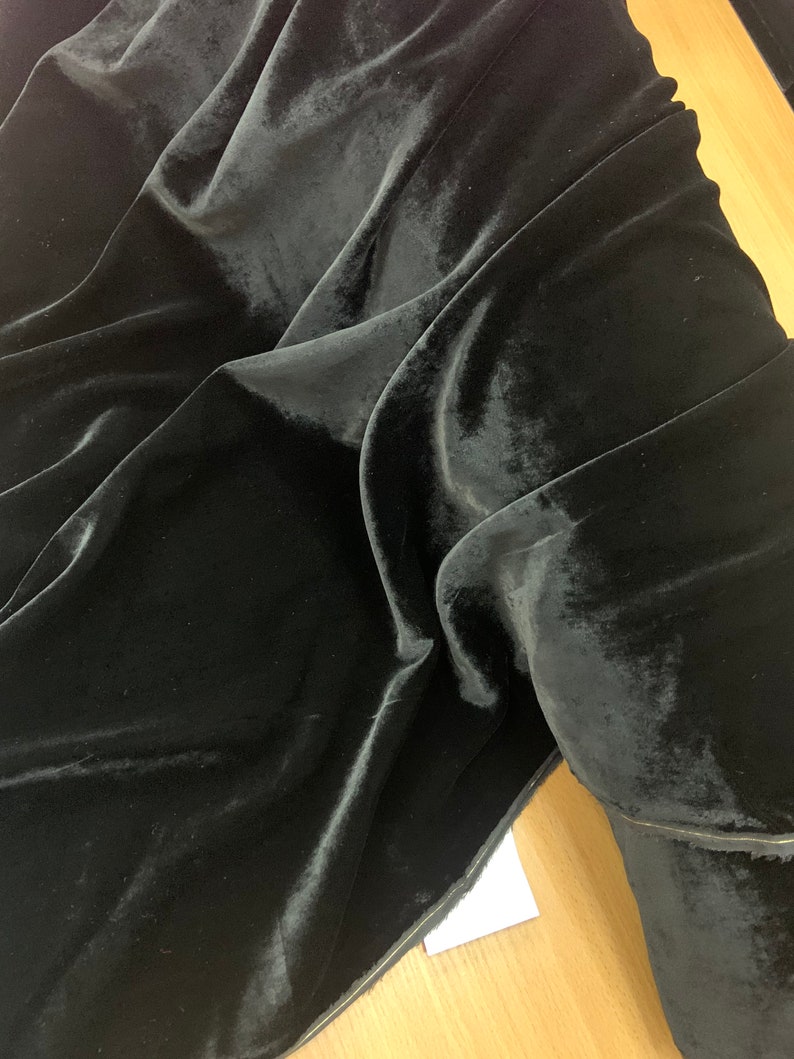 May include: Black velvet fabric with a smooth, soft texture. The fabric is folded and draped, showing its luxurious feel.