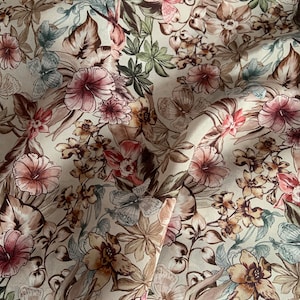 Op de afbeelding: Een beige stof met een bloemenprint met roze, bruine en groene bloemen, vlinders en bladeren.