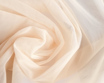 May include: A close-up of a soft, sheer, peach-colored fabric with a delicate texture. The fabric is draped and folded, creating a swirling pattern.