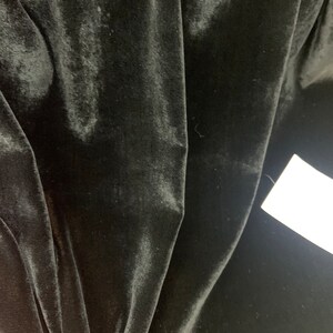 May include: Black velvet fabric with a smooth, soft texture. The fabric is folded and draped, showing its luxurious feel.