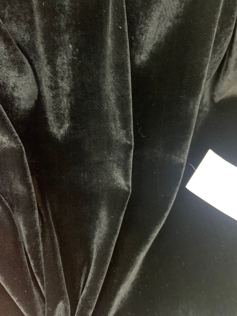 May include: Black velvet fabric with a smooth, soft texture. The fabric is folded and draped, showing its luxurious feel.