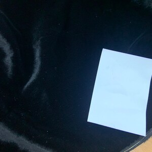 May include: A close-up of black velvet fabric with a white piece of paper on top. The fabric has a slight sheen and is smooth to the touch.