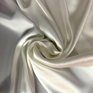 Puede incluir: Primer plano de una tela de satén blanco lisa. La tela está drapeada y doblada, creando líneas suaves y fluidas.