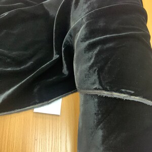 May include: Black velvet fabric with a subtle sheen. The fabric is folded and rolled, showing the texture and drape.