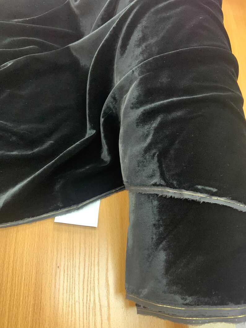 May include: Black velvet fabric with a subtle sheen. The fabric is folded and rolled, showing the texture and drape.