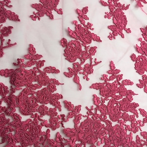 Può includere: Tessuto di pizzo floreale color borgogna con un delicato motivo di fiori e foglie. Il pizzo è su uno sfondo di rete trasparente.