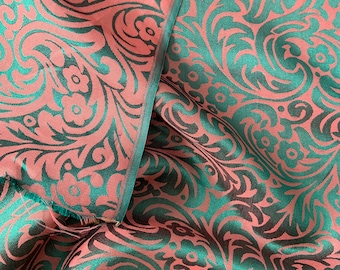 Könnte beinhalten: Nahaufnahme eines Stoffes mit einem sich wiederholenden Muster aus grünen und rosafarbenen Wirbeln und floralen Designs.