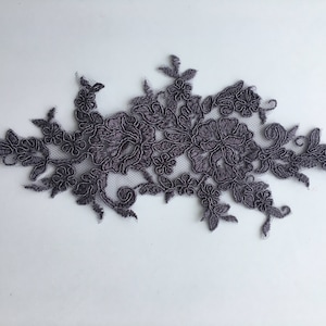 May include: A grey lace applique featuring a floral design. The lace is delicate and intricate, with a variety of flower shapes and sizes.