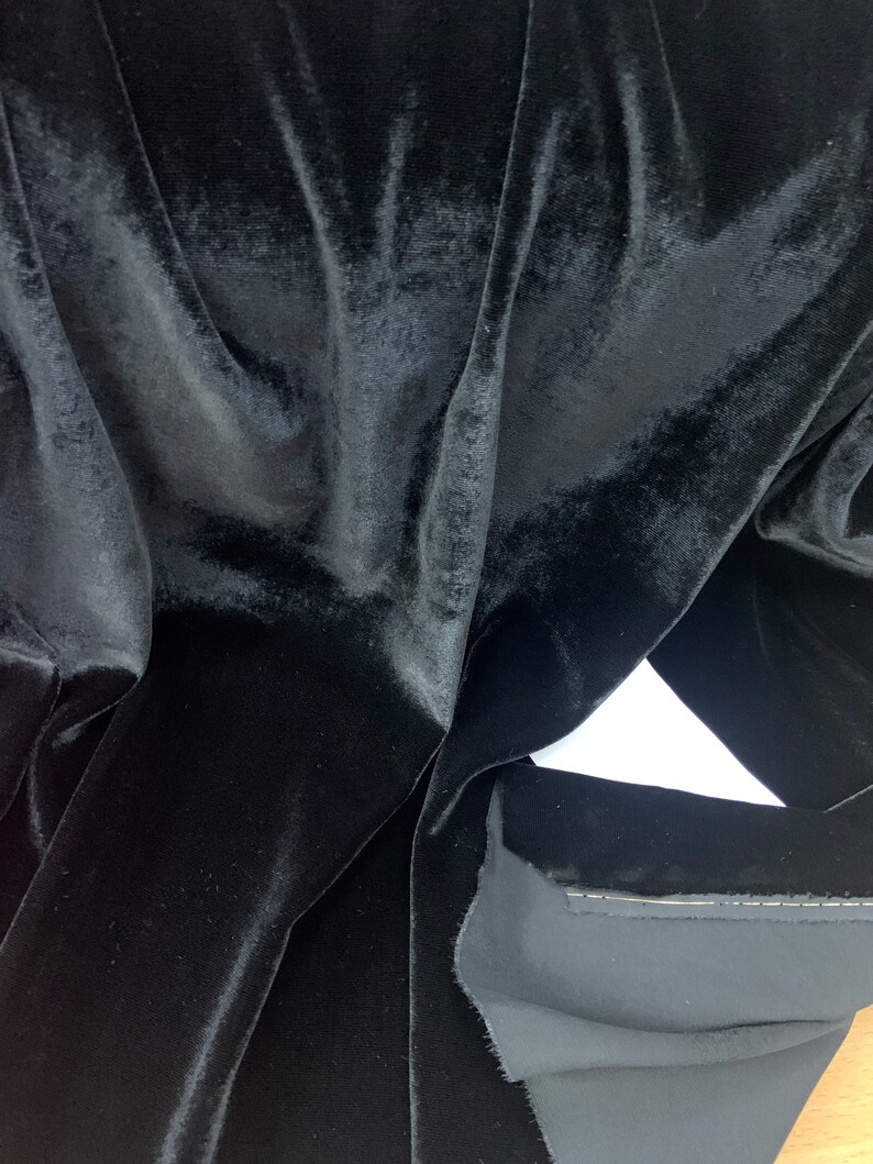 May include: Black velvet fabric with a smooth, soft texture. The fabric is folded and draped, showing the rich, deep color.
