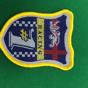 Könnte beinhalten: Ein blauer und goldener gestickter Aufnäher mit einem karierten Muster, einem silbernen Podest, einem Drachen und dem Wort "Racing".