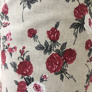 May include: Beige fabric with a repeating pattern of red roses and green leaves.