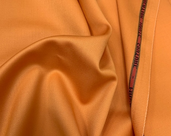 Könnte beinhalten: Nahaufnahme eines glatten, orangefarbenen Stoffes mit einem braunen und roten Band, auf dem "CREATION - HOUTLLE - COLORKE - MADE" steht.