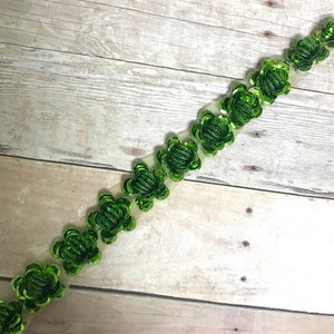 May include: Green sequined flower trim on a sheer white mesh ribbon. The trim is made of small, green sequins that are sewn together to form flower shapes.