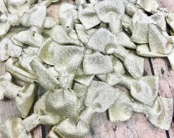 May include: A pile of gold-colored fabric bows. The bows are made of a textured material and are arranged in a random pattern.