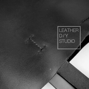 May include: Close-up of a black leather tote bag with a stitched seam and the text "LEATHER D/Y STUDIO" in a white rectangle.