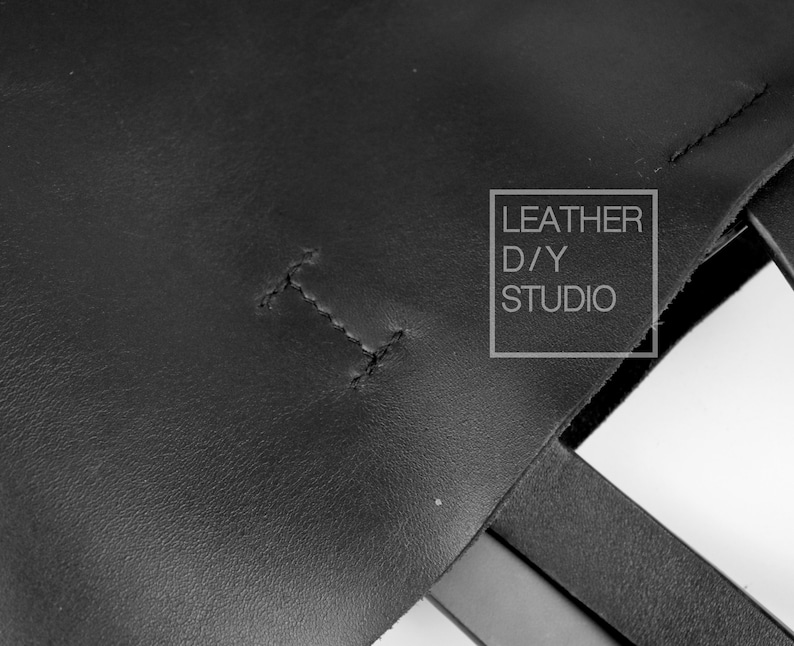 May include: Close-up of a black leather tote bag with a stitched seam and the text "LEATHER D/Y STUDIO" in a white rectangle.