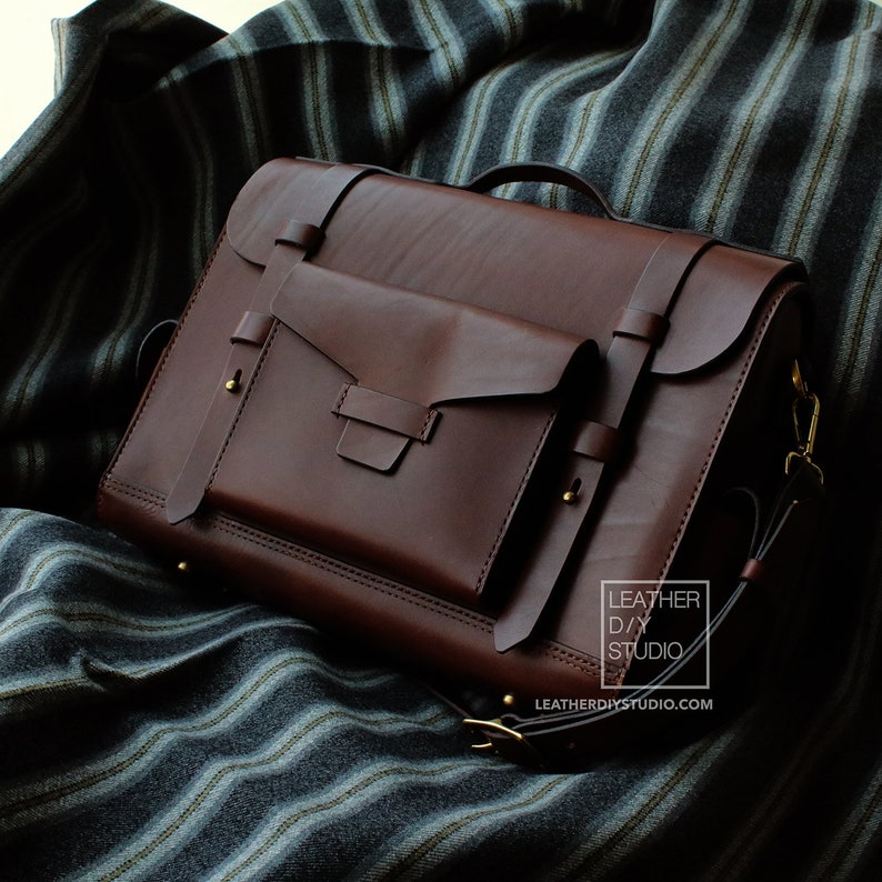 Puede incluir: Un malet&iacute;n de cuero marr&oacute;n con cierre de solapa y un bolsillo m&aacute;s peque&ntilde;o en la parte delantera. El malet&iacute;n tiene una correa y herrajes de color dorado. El texto "LEATHER DIY STUDIO" y "LEATHERDIYSTUDIO.COM" est&aacute; impreso en la esquina inferior derecha de la imagen.