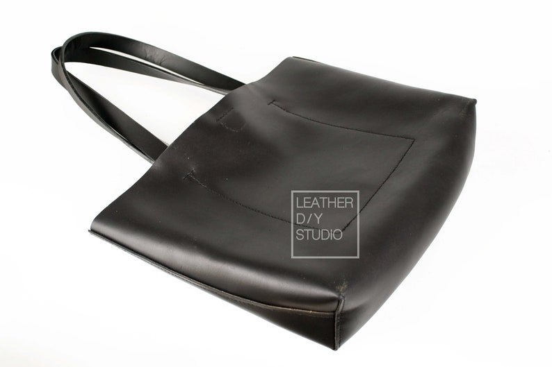 May include: A black leather tote bag with double straps. The bag has a small pocket on the front and the text "LEATHER D/Y STUDIO" is printed on a white rectangle.