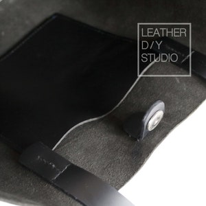 May include: A black leather tote bag with a black leather pocket on the inside. The bag has a snap closure and two black leather handles. The text "LEATHER D/Y STUDIO" is printed on a white rectangle on the bag.