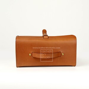 May include: A brown leather bag with a top handle and a buckle closure. The bag has a label that reads "LEATHER DIY STUDIO" and a website address: www.leatherdiystudio.com.